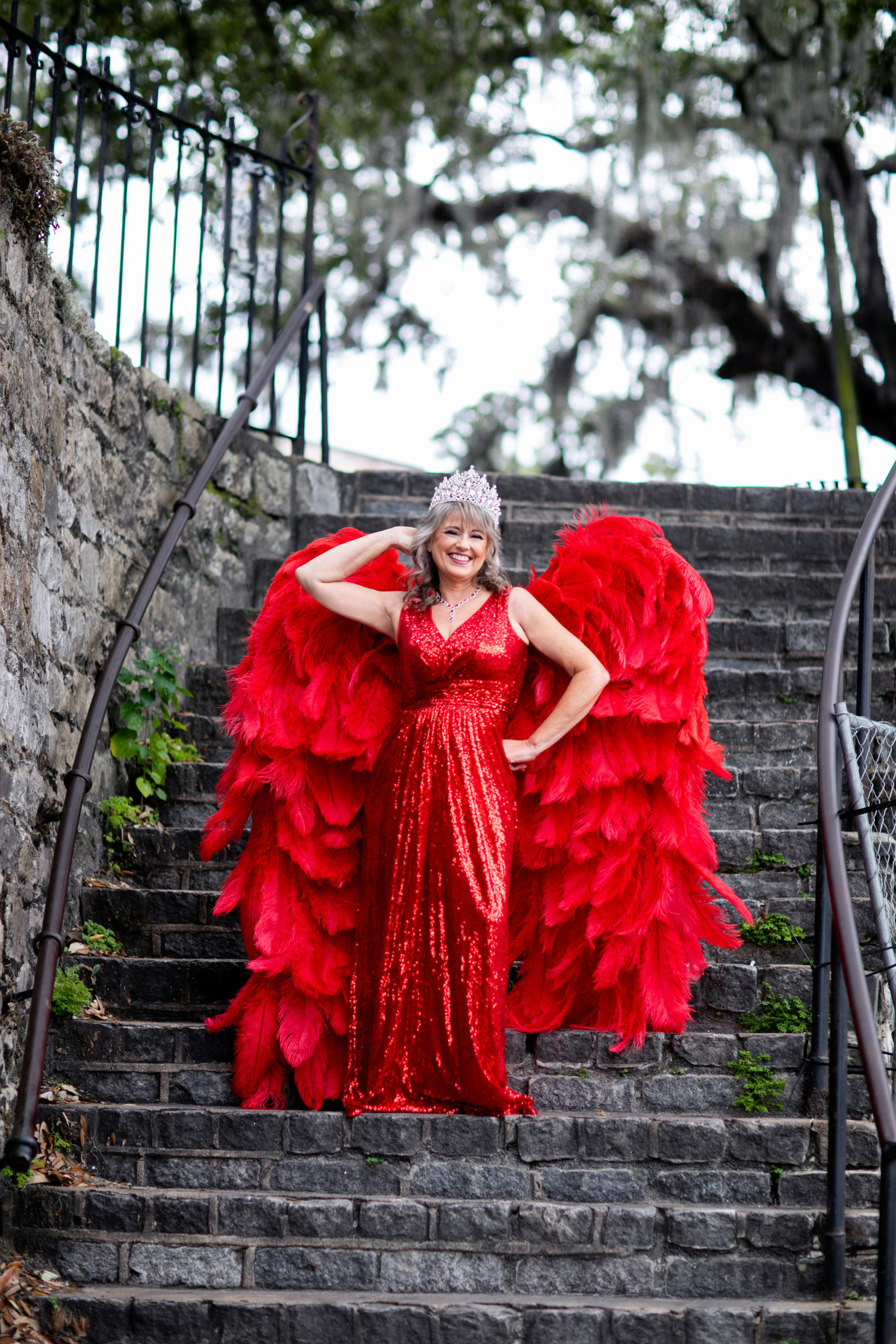 woman posed on stairs wearing red gown and angel wings
