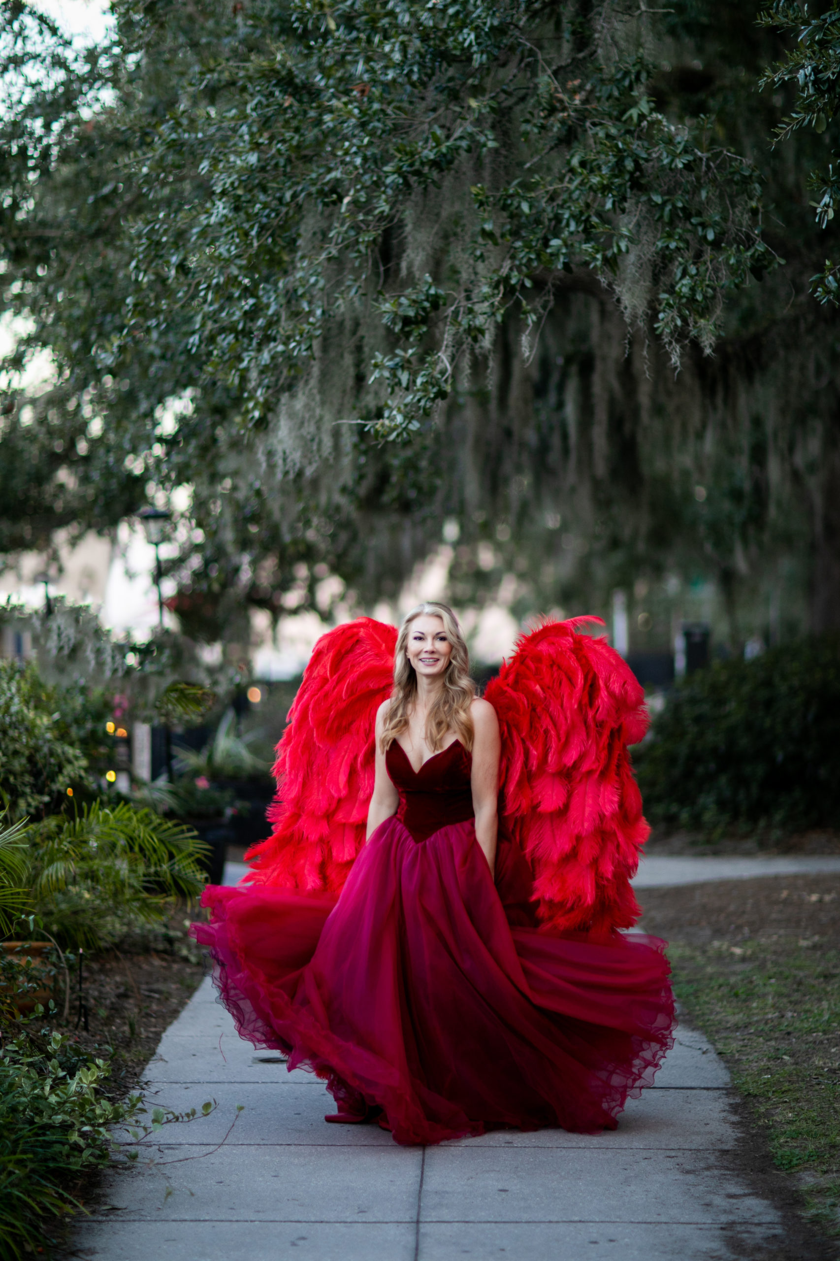 woman posing for outdoor portrait wearing red angel wings and gown