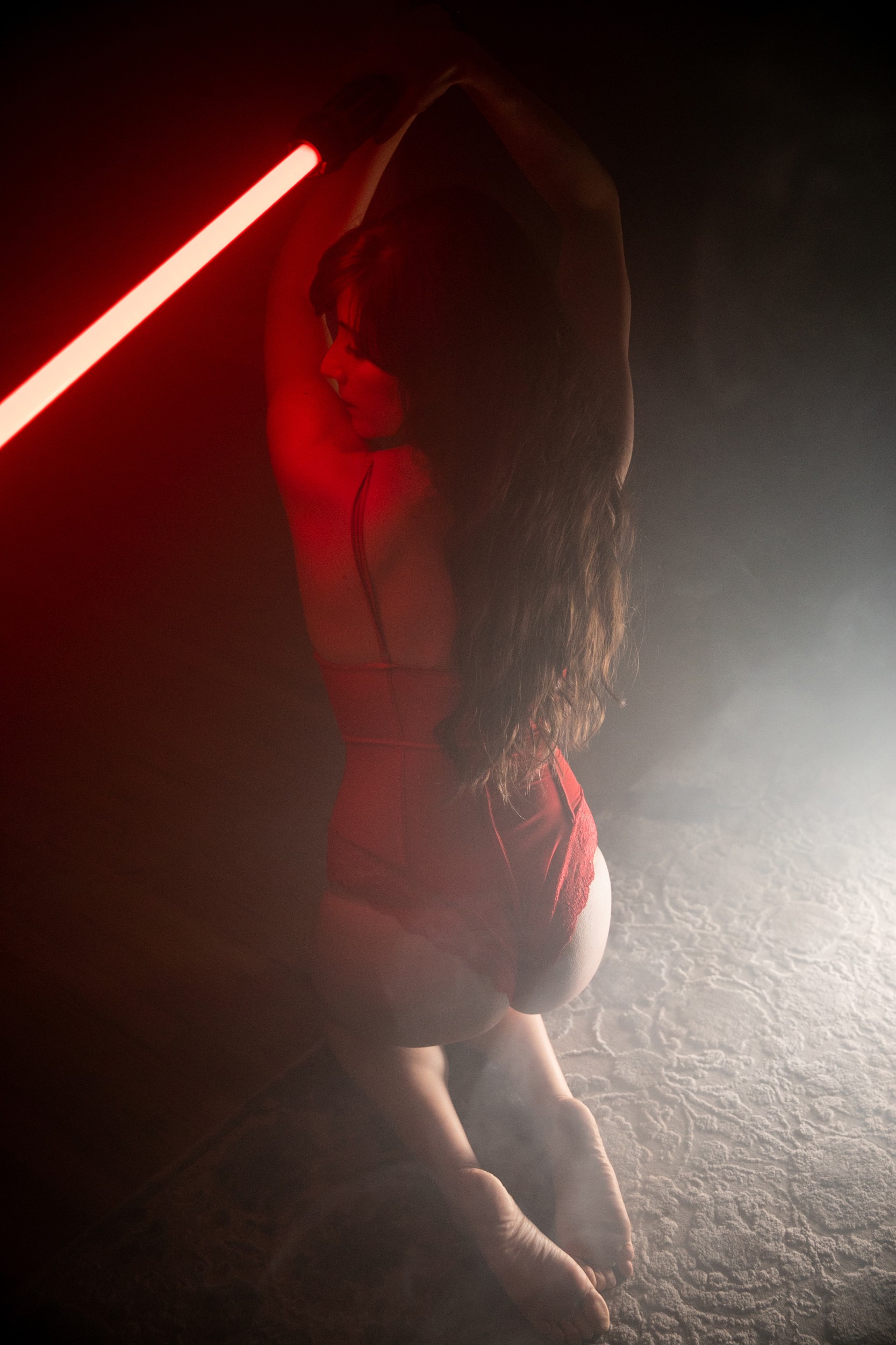 portrait of woman kneeling on ground in lingerie holding lightsaber
