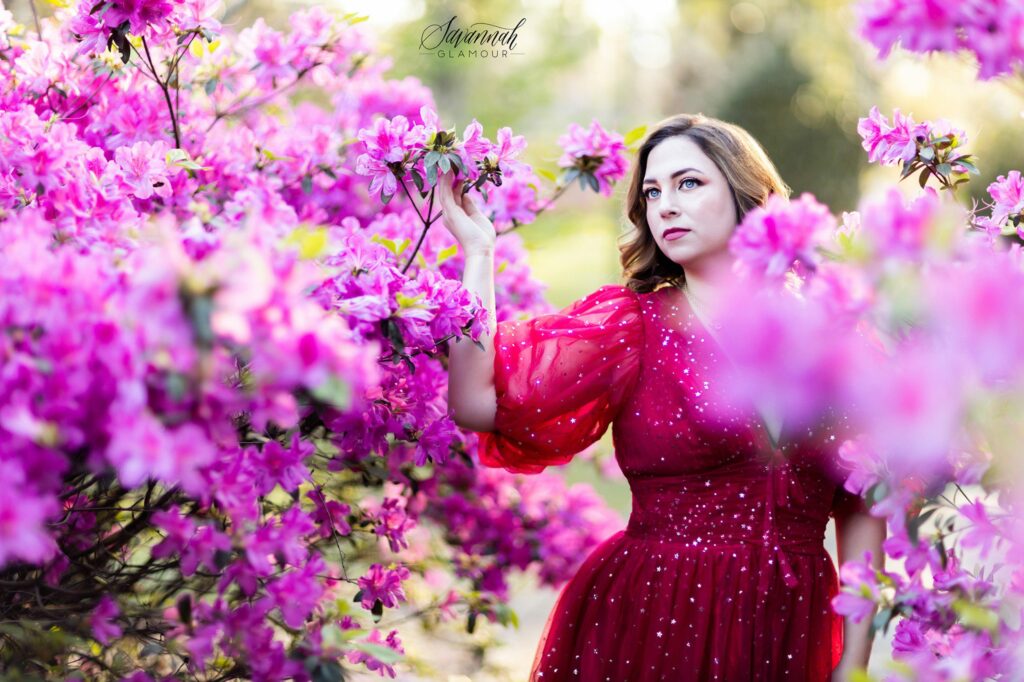 woman in a red glamour gown standing between two azalea bushes in Savannah, Georgia