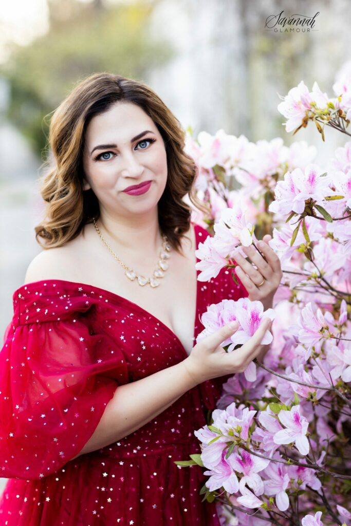 woman in a red glamour gown in front of an azalea bush in Savannah