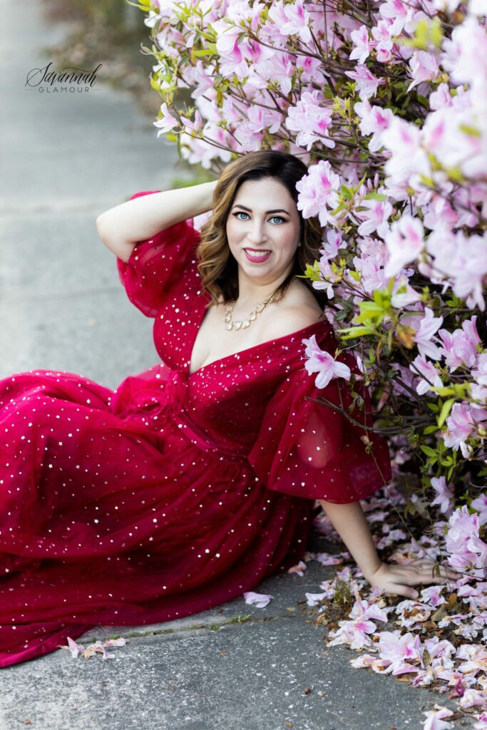 woman in a red glamour gown in front of an azalea bush