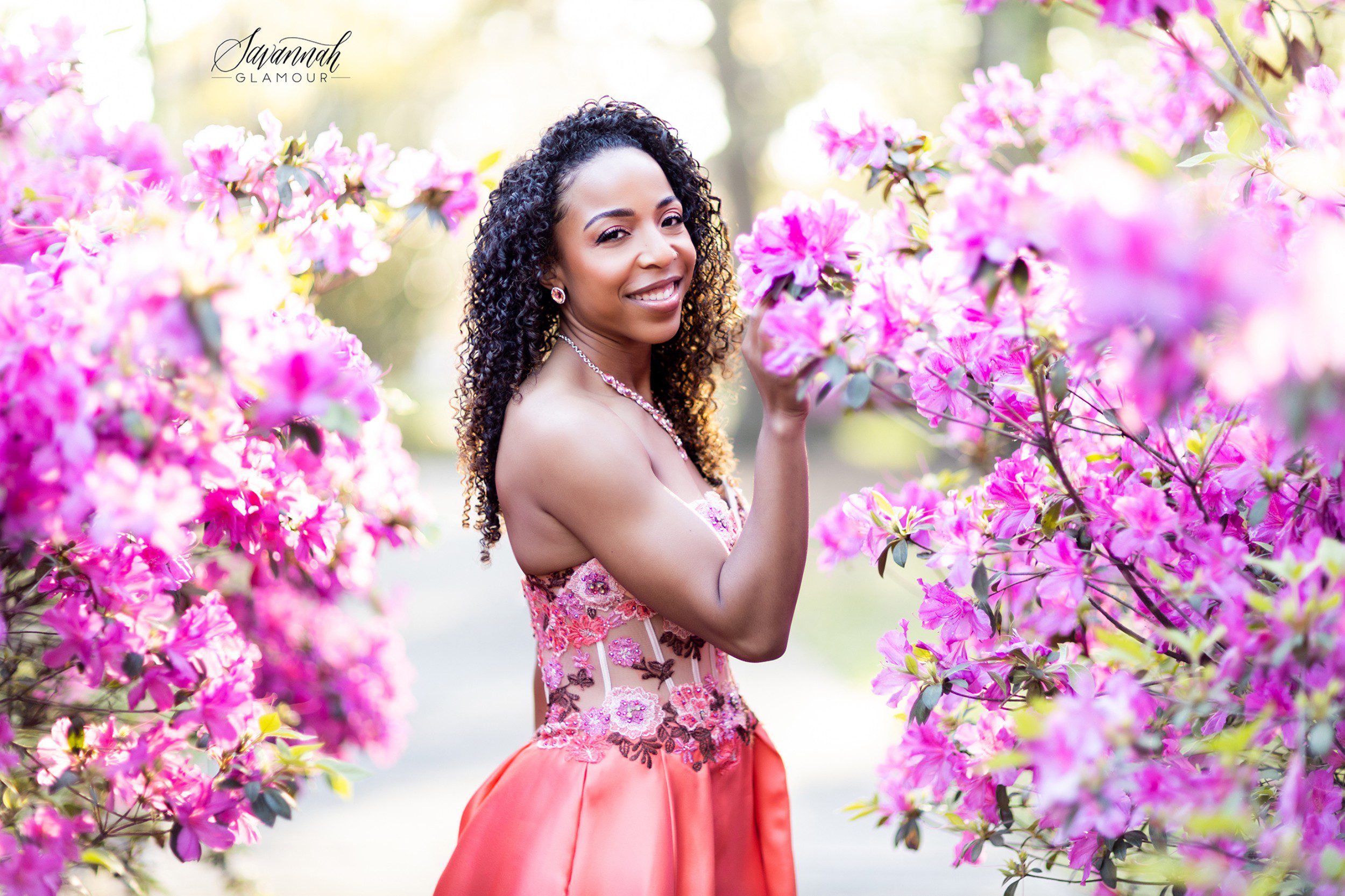A young woman in a pink dress posing in front of pink flowers.