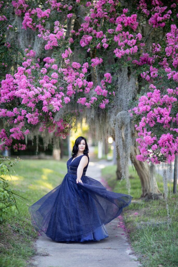 a woman in a glamourous gown posing outdoors in front of a pink flowering tree in Savannah, GA