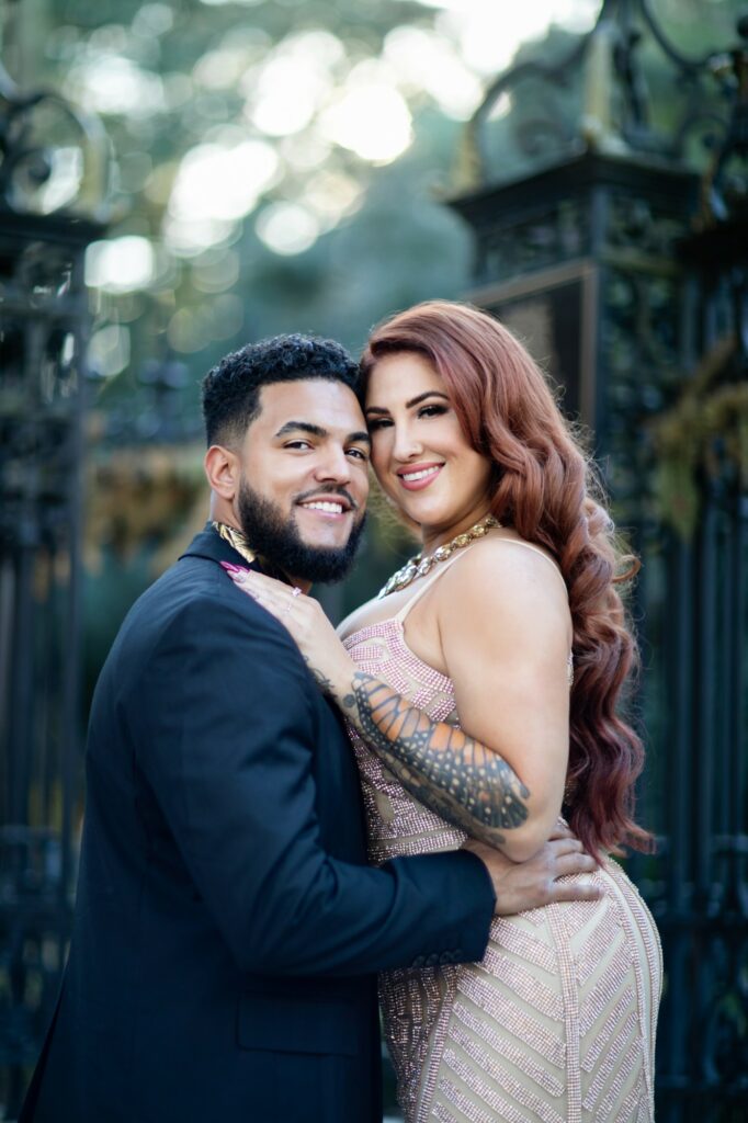 a couple in glamorous clothing embracing and smiling at the camera