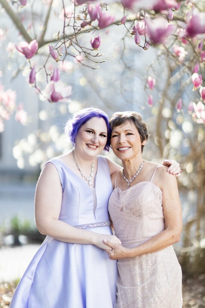 a mother and daughter in beautiful gowns post under a cherry blossom tree