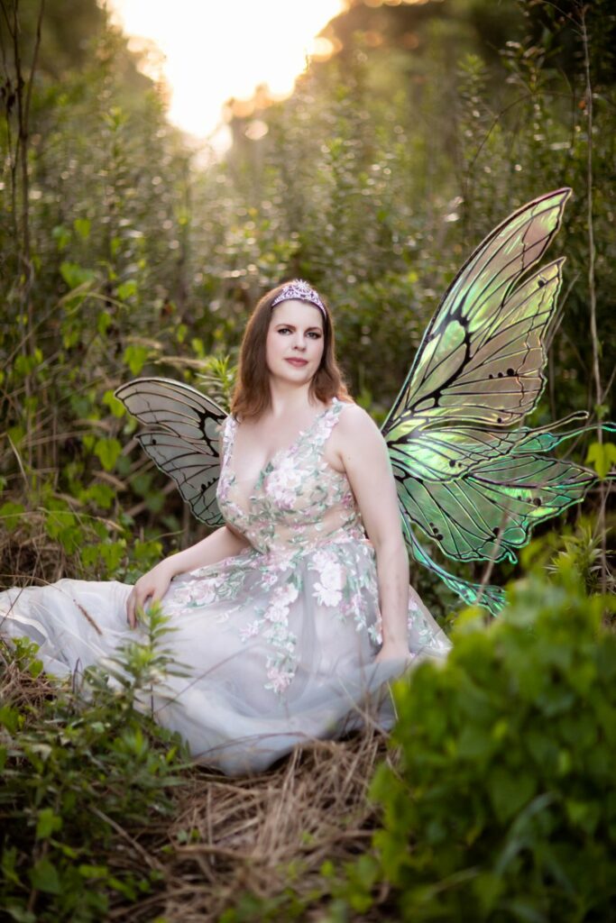 a woman in a glamorous gown and wings sitting in a forest